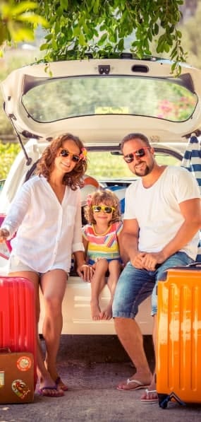 Parents and child by their car with suitcases